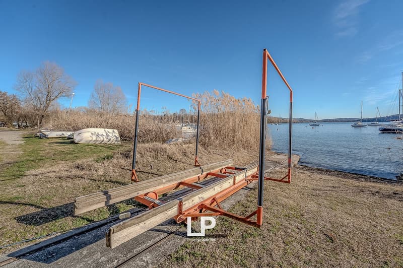 boat ramp, grassy area, water body, boats, trees, clear sky