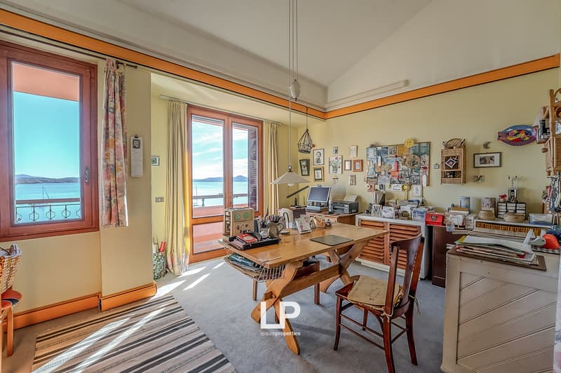 large windows, wooden desk, wooden chair, carpet, various items on the desk, shelves with items