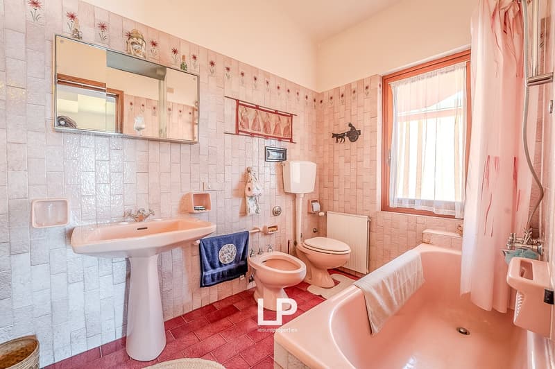 Bathroom with pink tiles, white sink, bidet, toilet, bathtub, mirror, towel rack, radiator, window with curtains