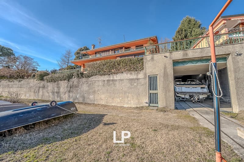 House with garage, boat in the garage, boat outside, concrete wall, trees