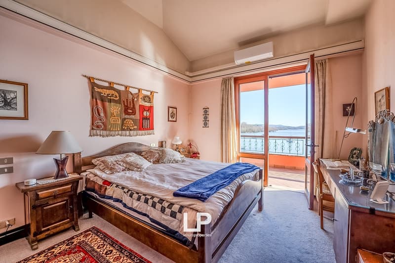large bed, nightstands, lamp, rug, air conditioner, balcony, window, desk, chair, mirror, framed pictures, curtain