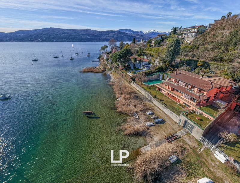 House on the lake shore, red roof, swimming pool, several boats docked, mountain view