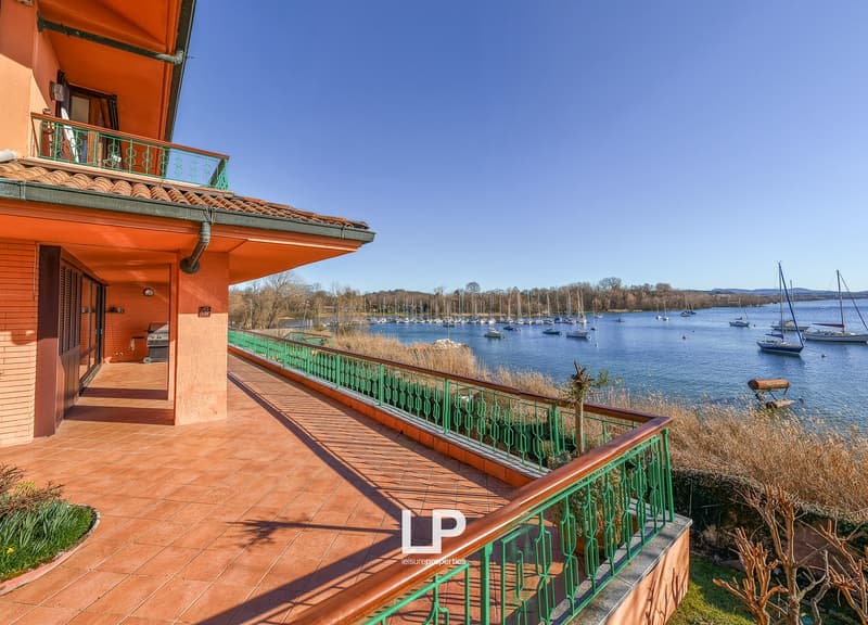 Terrace with green railings, tiled floor, view of the lake, several boats docked