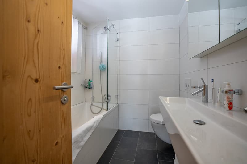 Bathroom with bathtub, shower, toilet, sink, mirror, wooden door