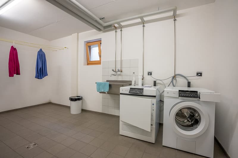Laundry room with washing machine, dryer, sink, and trash bin.