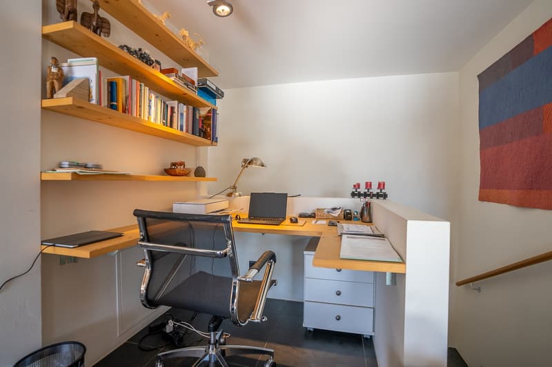desk with chair, shelves with books, printer, lamp, papers, cup, pen holder, trash can