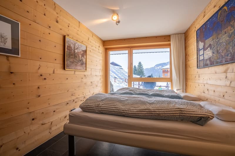 bedroom with wooden walls, bed, two pillows, two blankets, large window with view of mountains