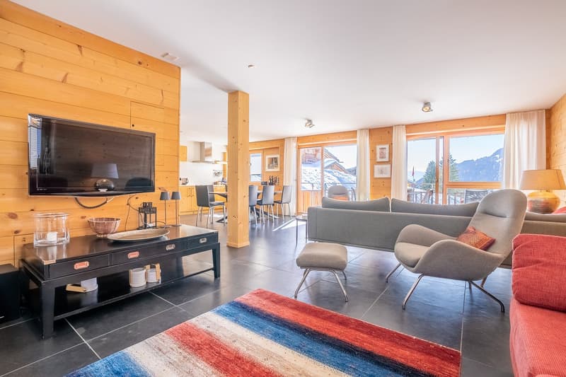 wooden wall, flat screen TV, coffee table, sofa, armchair, rug, dining table, chairs, kitchen, windows