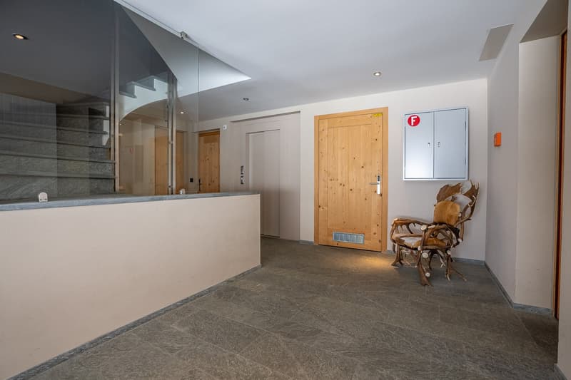 Empty room with tiled floor, wooden door, glass wall, staircase, and a chair