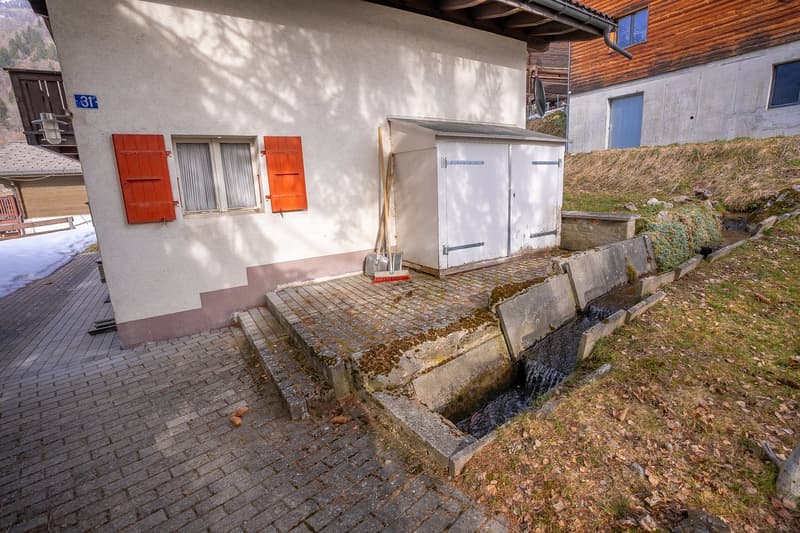 white house with red shutters, small window, small door, small brick path, small water channel, small shed