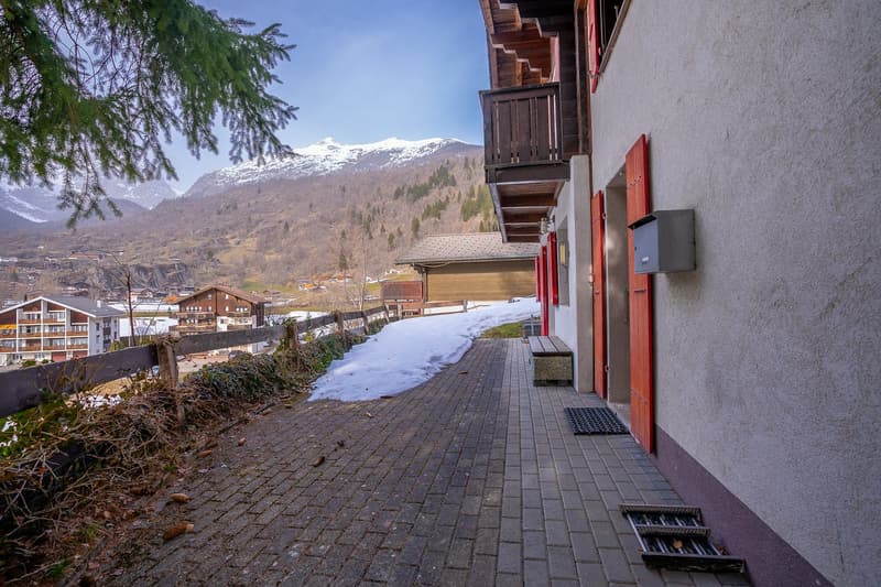 brick walkway, wooden fence, red doors, balcony, snow on ground, mountain view