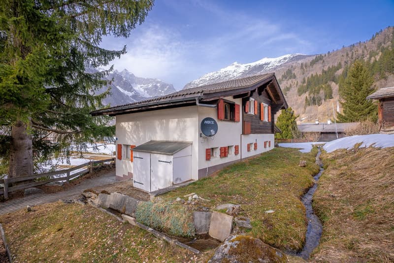 Mountain house, white exterior, red shutters, satellite dish, small garden, snowy mountains in the background