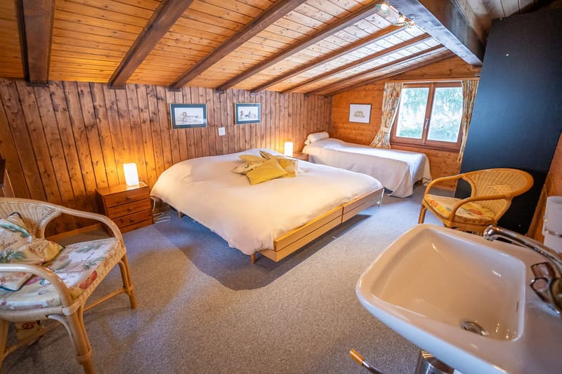 bedroom with two beds, wooden walls, carpeted floor, nightstands, lamps, chairs, sink, window with curtains