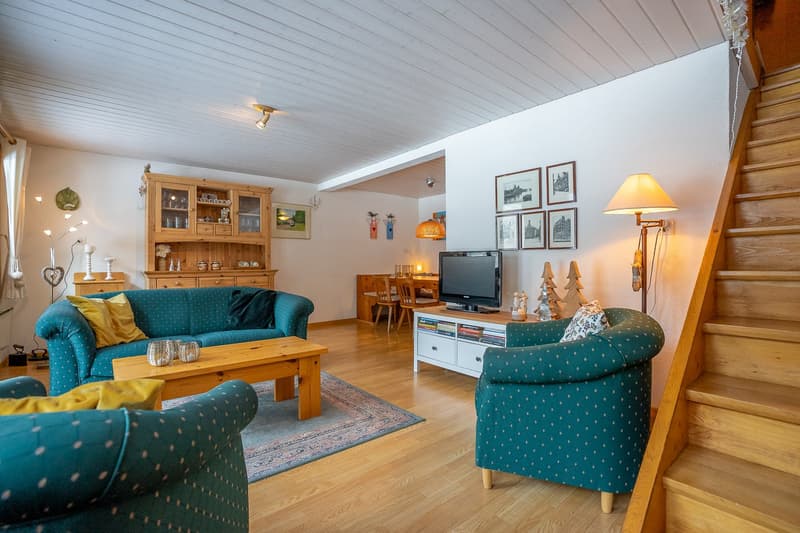 living room with wooden floor, wooden coffee table, blue sofas, wooden cabinet, TV, lamp, carpet, wooden stairs