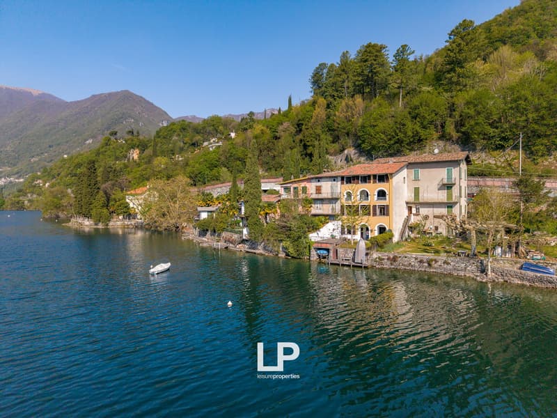 House on the lake shore, surrounded by trees and mountains, with a small boat in the water