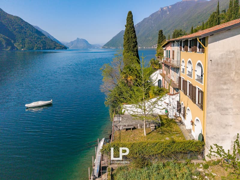 House on the lakefront, yellow and white exterior, balcony, boat dock, mountains in the background