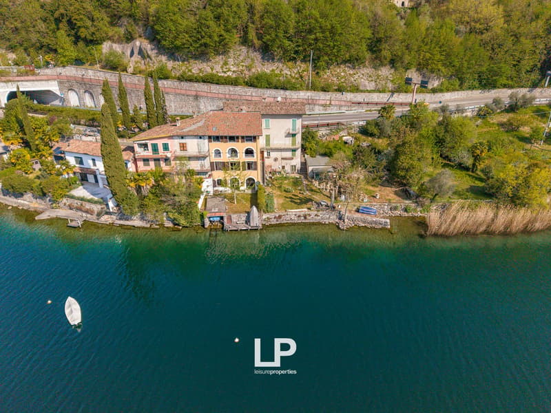 House on the lake, surrounded by trees, with a dock, and a road nearby