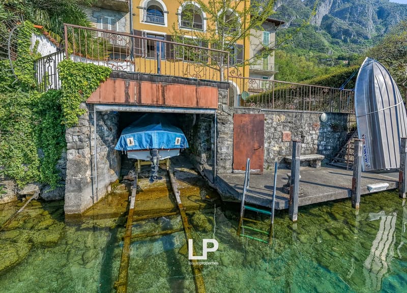 House with a boat dock, yellow exterior, stone walls, boat covered with a tarp, mountains in the background