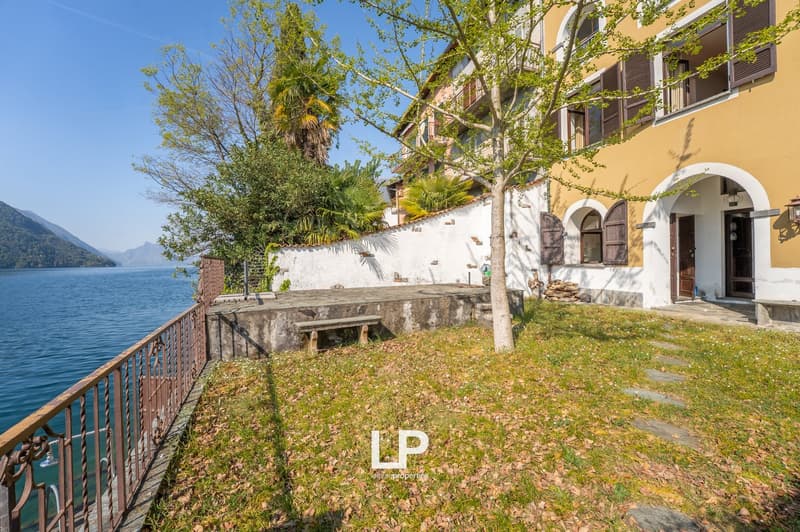 House with yellow walls, white wall, balcony, bench, tree, grass, lake, mountains