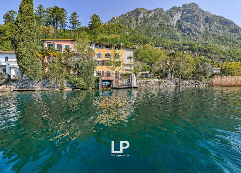 House on the lake, surrounded by trees, mountains in the background, yellow and pink facades