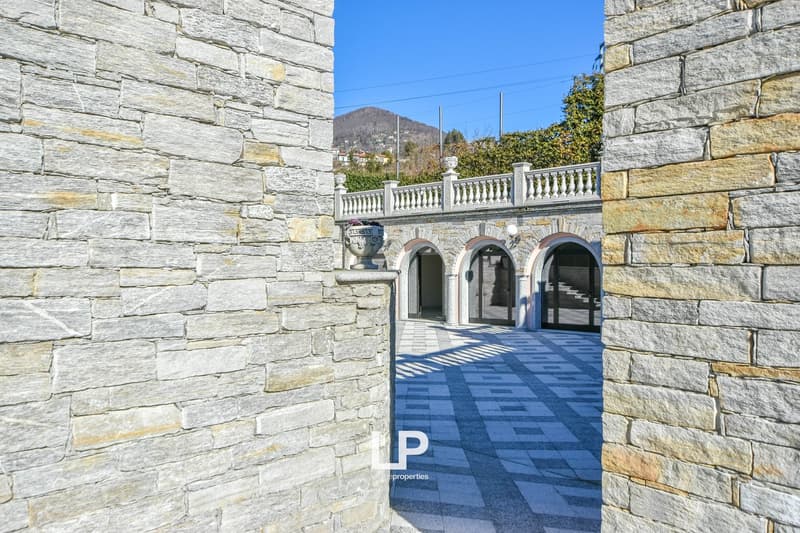 Stone walls, arched entrance, balcony, decorative urn, paved courtyard