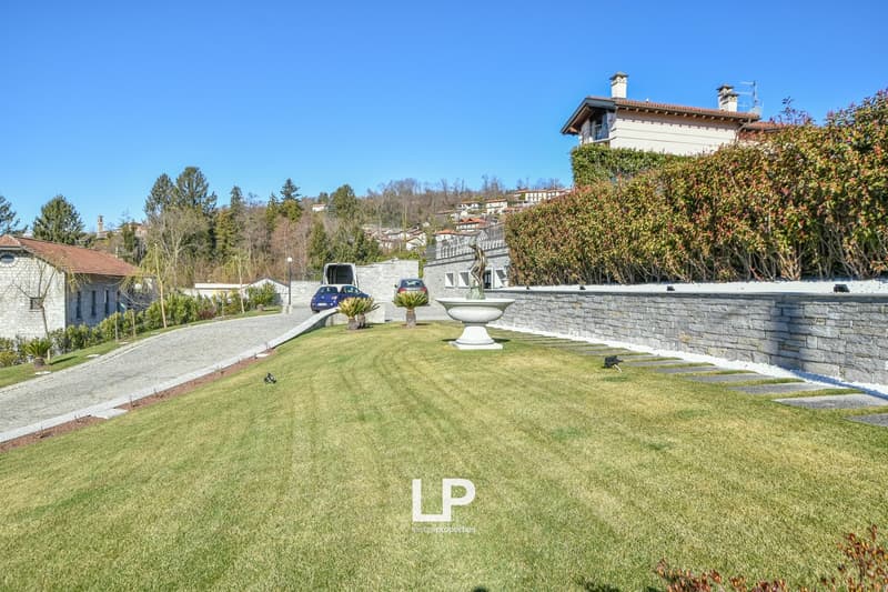 Stone wall, grassy lawn, decorative fountain, paved driveway, hedge, stone pathway