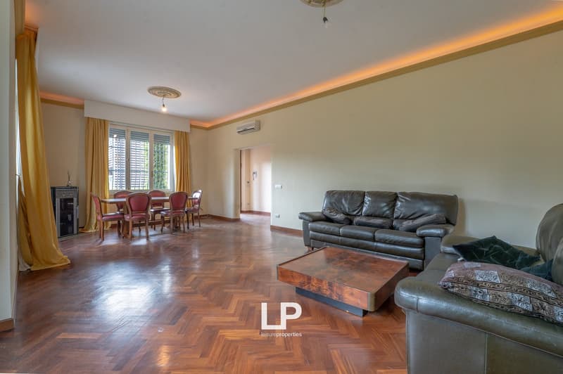 living room with wooden floor, two leather sofas, wooden coffee table, dining table with chairs, fireplace, windows with curtains