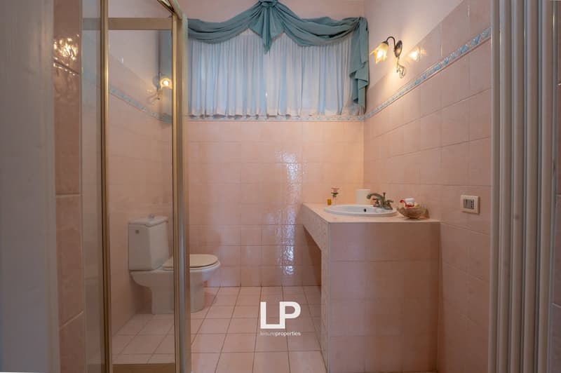 Bathroom with white toilet, shower enclosure, sink, and tiled walls and floor.