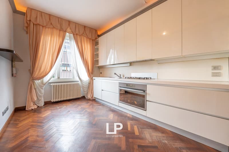 modern kitchen with wooden floor, white cabinets, gas stove, oven, radiator, window with curtains