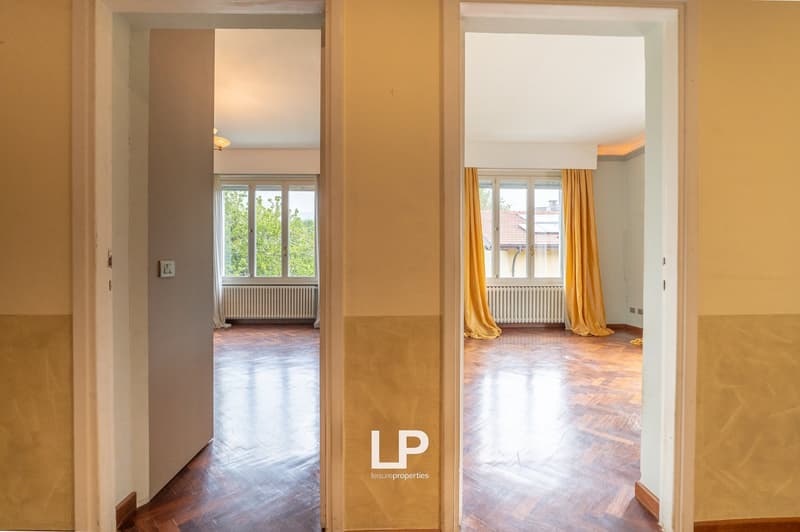 Empty room with wooden floor, two windows with yellow curtains, radiators, and a ceiling lamp.