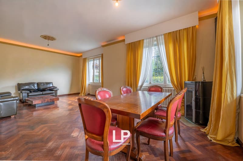 dining room with wooden table, red chairs, yellow curtains, wooden floor, leather sofa, coffee table, radiator, windows