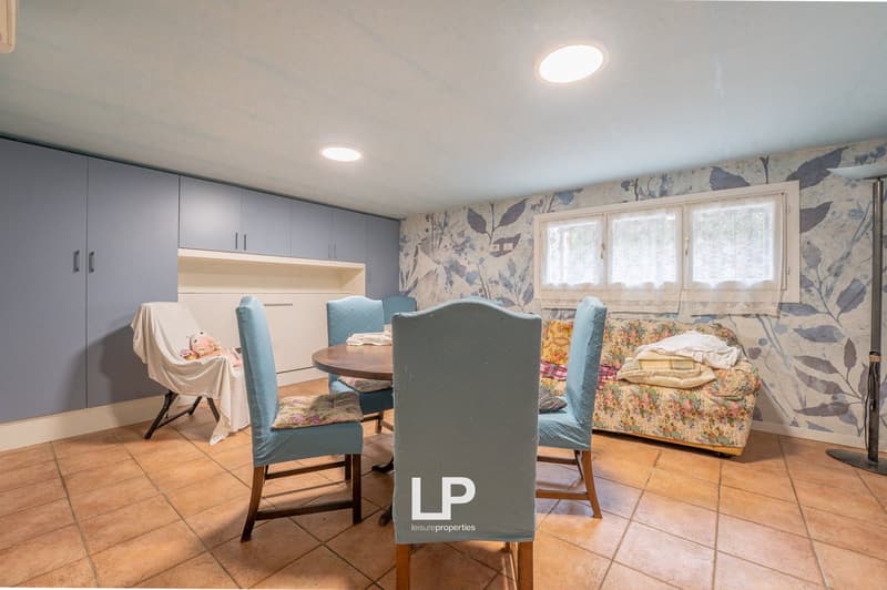 Dining room with wooden table, blue chairs, floral couch, blue cabinets, tiled floor, windows with white curtains
