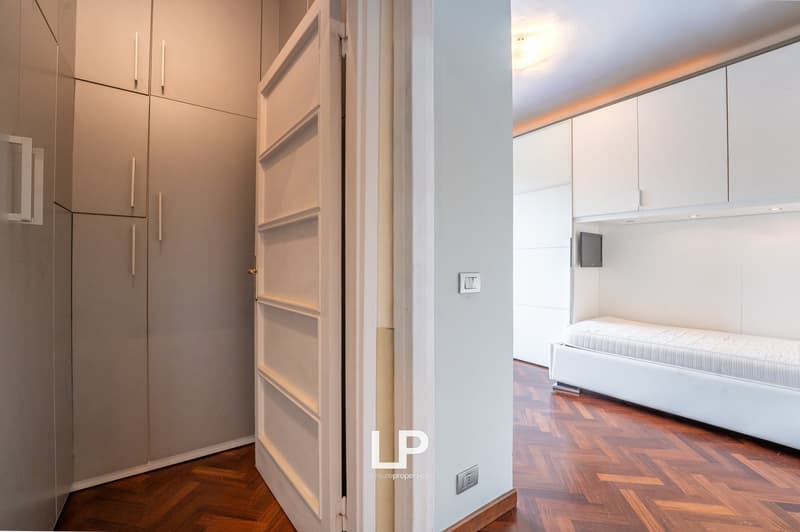 wooden floor, white walls, built-in wardrobes, open door, white bed, white cabinets, light switch, power outlet