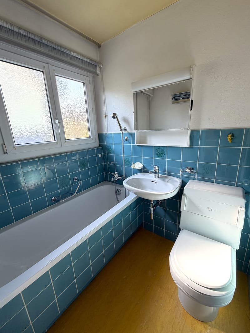 Bathroom with blue tiles, bathtub, sink, toilet, and a window