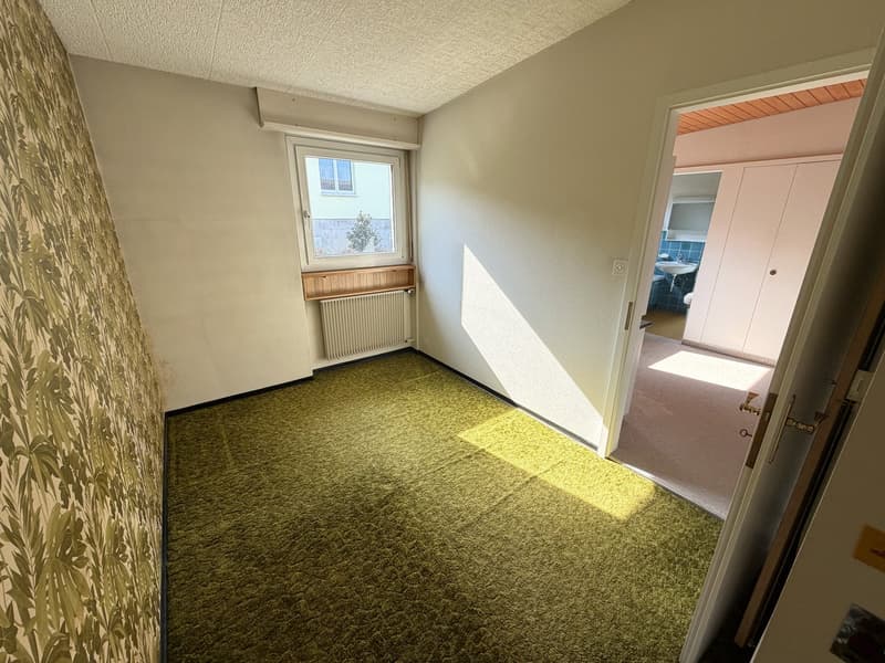 empty room, green carpet, white walls, window with wooden frame, radiator, open door