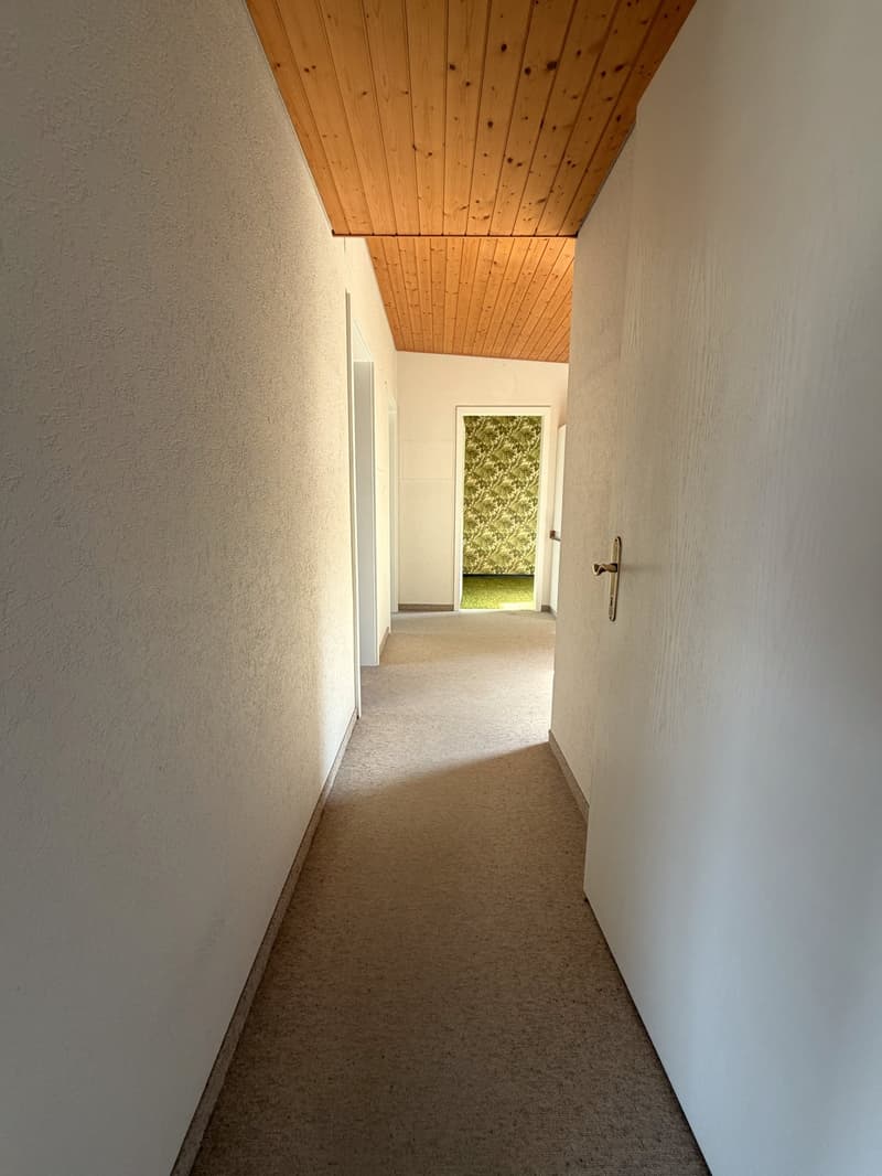 Empty hallway with wooden ceiling, carpeted floor, white walls, and doors leading to rooms.