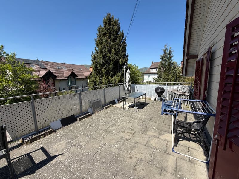 tiled floor, metal railing, table, chairs, grill, closed umbrella, view of houses and trees