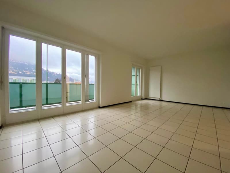 White tiles, sliding doors to a balcony with green railings, large windows with views of the city and mountains