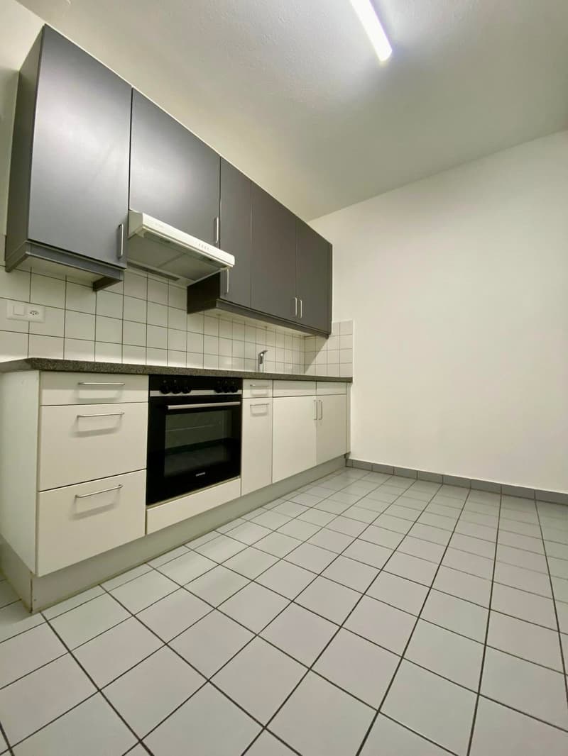 Empty kitchen with tiled floor, white cabinets, integrated oven, and stovetop, and a white tiled wall.