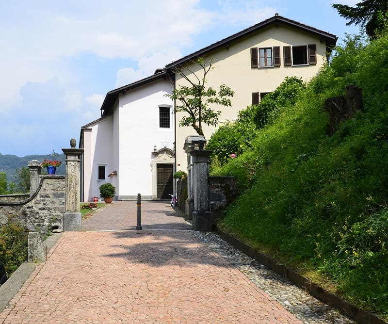 Two story house, elevated entrance, brick driveway, small stone fence, green shrubbery, wooden door, flower vase