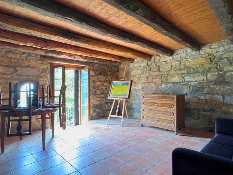 living room with stone walls, wooden beams, painting on easel, sofa, table, chairs, floor tiles