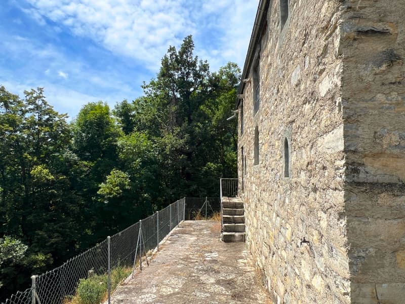stone wall house, slopping side of a mountain, fenced entrance, stairs to entrance