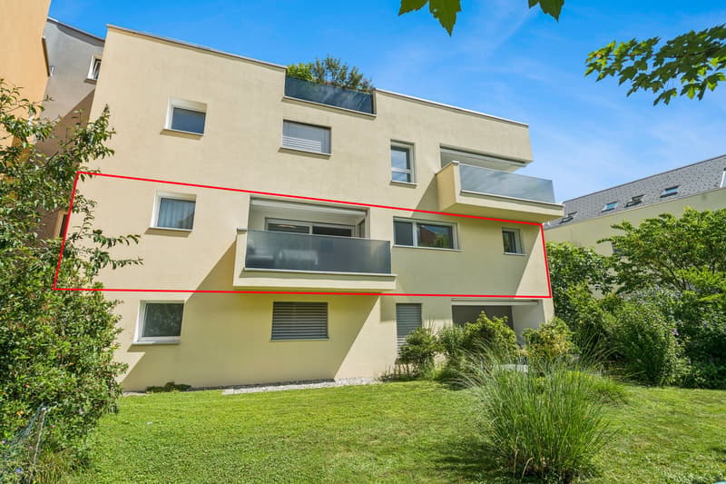 Beige apartment building, two-story house with two balconies, garden in front of the building