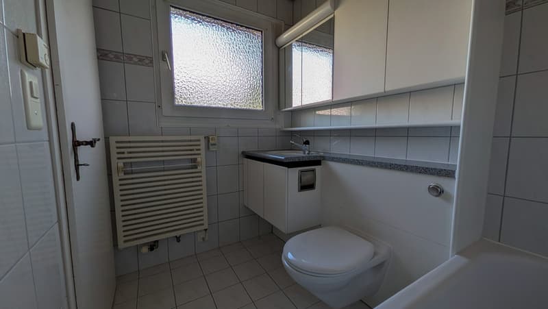 Bathroom with white tiles, white toilet, white sink, white cabinets, window, and a towel radiator.