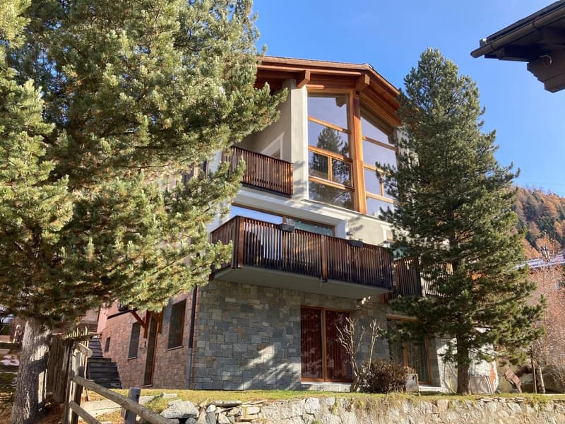 House made of stone and glass, large windows, wooden balcony