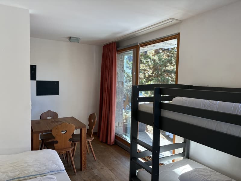 Wooden floors, bunk bed, small dining table with chairs, sliding door, and red curtains, wall-mounted TV