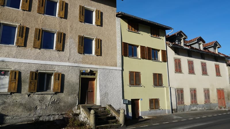 Three buildings side by side, each with multiple windows, wooden shutters, and entrances, made of concrete.