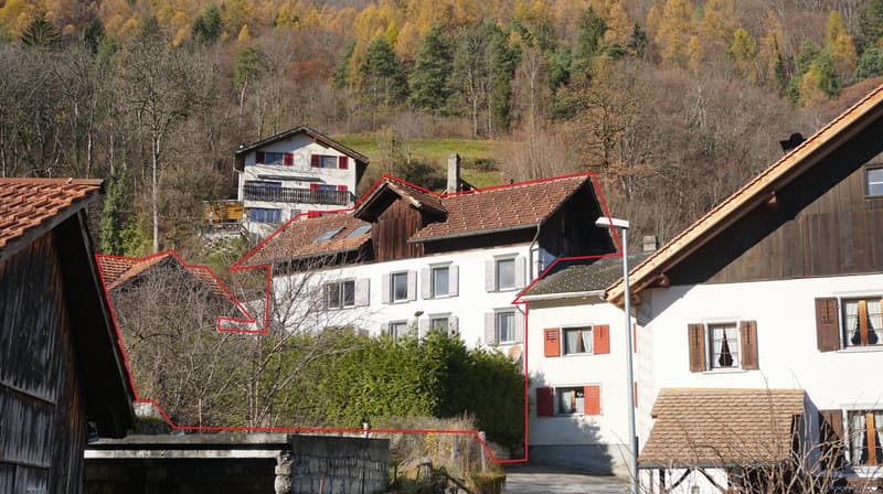 Multi-story residential building in a rural area, red-lined outline, surrounded by trees, with tiled roof, chimney, and windows.
