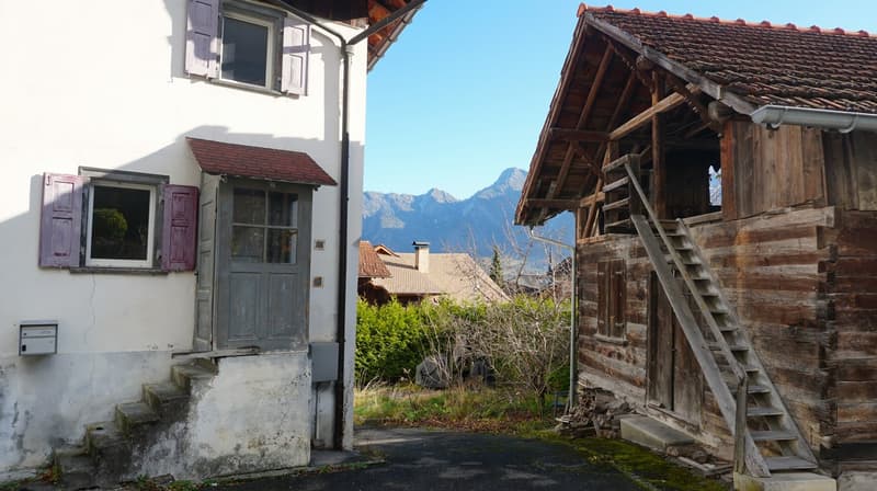 two buildings, white and wooden, concrete driveway, mountain in background