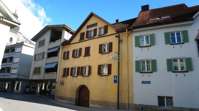Three-story building with yellow facade, brown wooden door, multiple windows with shutters, blue sign, street light, and awnings
